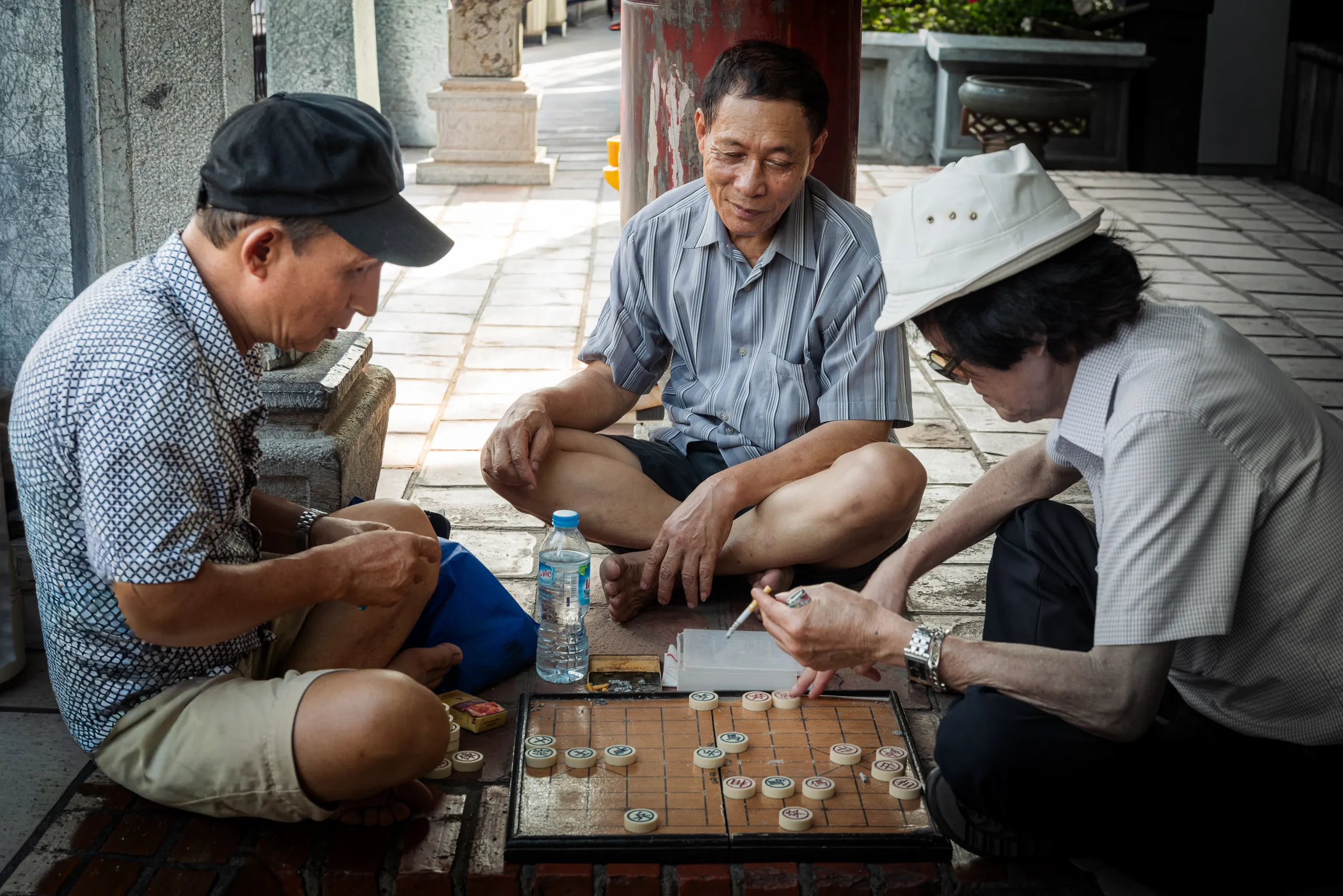 Three men gathered around a board game on a sidewalk in Vietnam